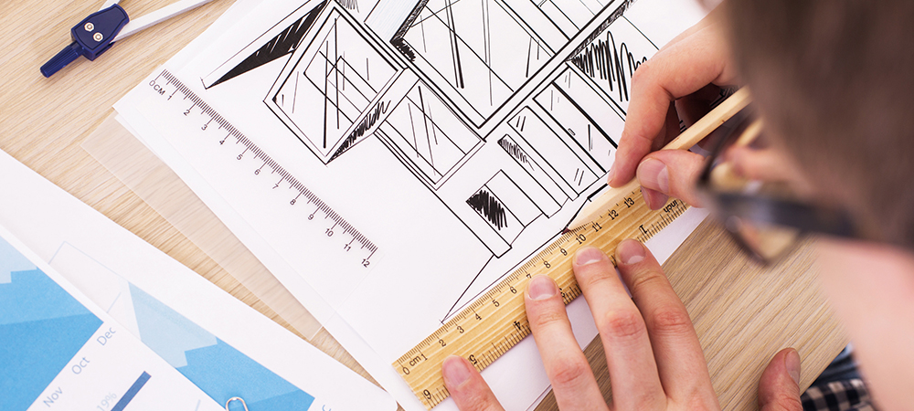 Top view of young architect using ruler and pencil to draw blueprint on wooden desktop with business report and a pair of compasses